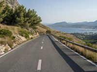 the road curves near some water with trees in it and mountains on either side of the road