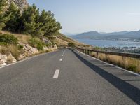 the road curves near some water with trees in it and mountains on either side of the road