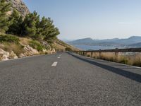 the road curves near some water with trees in it and mountains on either side of the road