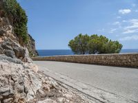 the asphalt road is made with stone in front of the sea view and trees near by