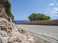 the asphalt road is made with stone in front of the sea view and trees near by