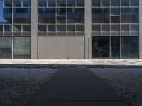 a tall building with large windows and a concrete path leading to the building and walkway