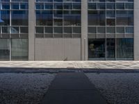 a tall building with large windows and a concrete path leading to the building and walkway