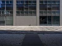 a tall building with large windows and a concrete path leading to the building and walkway