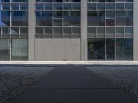 a tall building with large windows and a concrete path leading to the building and walkway