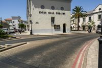 street scene with white building and palm trees on corner next to roadway and red curb