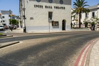 street scene with white building and palm trees on corner next to roadway and red curb