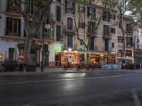 street view of people sitting at outdoor cafe tables, along road, in evening, with cars