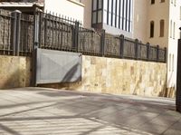 a man on a skateboard riding through a city street next to a building and fence