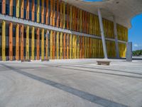 a concrete structure made into rows of orange and yellow poles are on a cement sidewalk