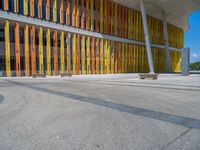 a concrete structure made into rows of orange and yellow poles are on a cement sidewalk