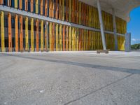 a concrete structure made into rows of orange and yellow poles are on a cement sidewalk