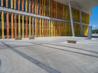 a concrete structure made into rows of orange and yellow poles are on a cement sidewalk