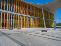 a concrete structure made into rows of orange and yellow poles are on a cement sidewalk