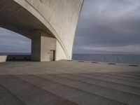 there is a building overlooking the ocean with some stairs on the bottom, and a person sitting in the middle of the room