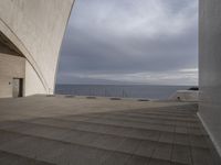 there is a building overlooking the ocean with some stairs on the bottom, and a person sitting in the middle of the room