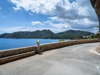 a road that has some rocks near the ocean by the mountains and water is blue