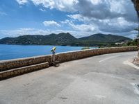 a road that has some rocks near the ocean by the mountains and water is blue