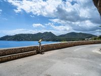 a road that has some rocks near the ocean by the mountains and water is blue