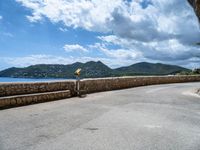 a road that has some rocks near the ocean by the mountains and water is blue