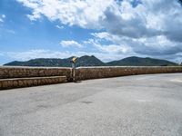 a road that has some rocks near the ocean by the mountains and water is blue