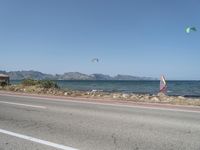 some kites are being flown on an empty road near the water on a beach