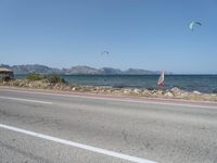 some kites are being flown on an empty road near the water on a beach