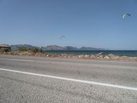 some kites are being flown on an empty road near the water on a beach