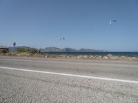 some kites are being flown on an empty road near the water on a beach