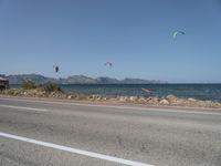 some kites are being flown on an empty road near the water on a beach