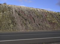 a white motorbike riding past a big stone wall on the road in the middle of nowhere