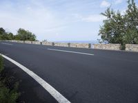 an empty road with a stone wall and blue sky behind it on a bright day