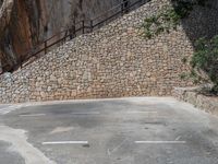 a man riding a motorcycle down a dirt road near a large rock wall and stone staircase