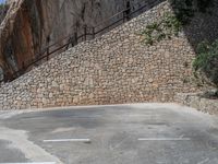 a man riding a motorcycle down a dirt road near a large rock wall and stone staircase