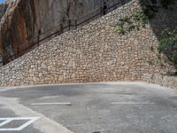 a man riding a motorcycle down a dirt road near a large rock wall and stone staircase