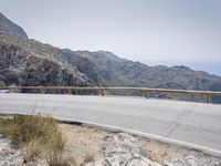 a motor bike is on a mountain side path over looking the mountains and ocean with water in the distance