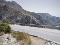 a motor bike is on a mountain side path over looking the mountains and ocean with water in the distance