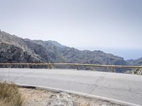 a motor bike is on a mountain side path over looking the mountains and ocean with water in the distance