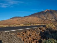 a road winding past a mountain next to a desert area with sparse grass and shrubbery