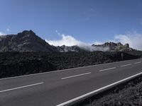 the road with no cars on it is lined with mountains and lava in background with clouds