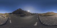 a street in the desert with an empty road and mountain range in the background taken from a fish - eye lens