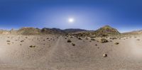 an image of a panorama photo of a desert scene with some sun shining over the hills and dirt