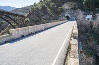 an empty roadway near the road leading to a cave on the mountain side with a tunnel and bridge