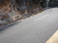 a motorcycle is riding down a curve road with rocky terrain behind it and some trees in the background