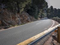 a motorcycle is riding down a curve road with rocky terrain behind it and some trees in the background