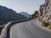 an empty asphalt road winds through a rocky area with mountains in the background and blue sky overhead