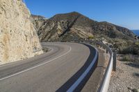 a curve in the side of a highway with mountain in background and blue sky overhead