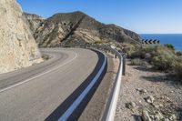 a curve in the side of a highway with mountain in background and blue sky overhead