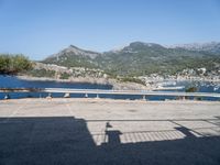 a shadow on the ground near a bridge near water and hills, some with mountains in the background