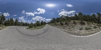 the camera lens is reflecting a curved road near trees and mountains in a 360 - panorama lens